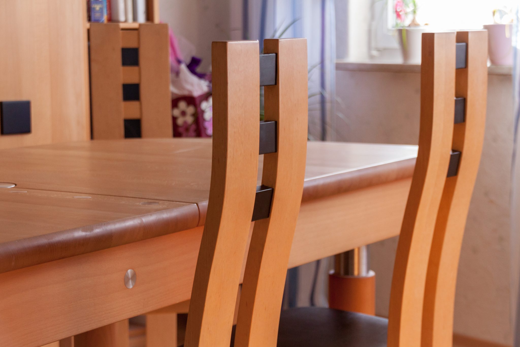Detailaufnahme der leicht gebogenen Rückenlehne zweier Stühle aus der Xen-Serie der Schreinerei. Die Stuhle stehen an einem Holztisch in passender Optik.