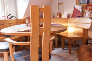 Nahaufnahme eines Stuhles aus hellem Holz, der an einem Tisch mit Eckbank steht.